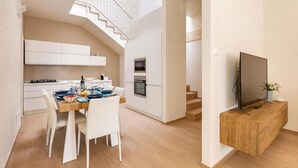 Una cuina moderna amb armaris blancs, una taula de dinar preparada per a quatre persones i un televisor sobre un suport de fusta.