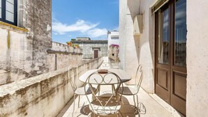A narrow outdoor patio with a round table and four chairs, a concrete wall, and a building with a window and door. - 2043 Antica Dimora Stasi by Barbarhouse (Presicce-Acquarica)