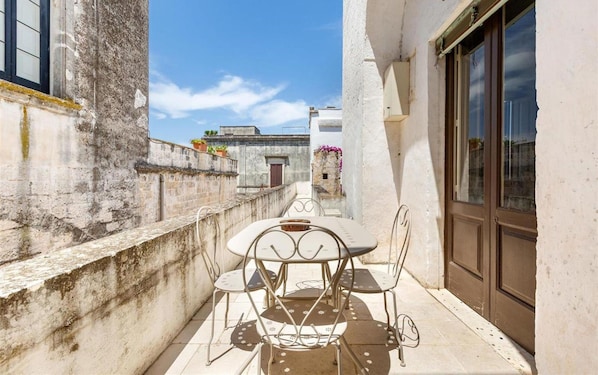 A narrow outdoor patio with a round table and four chairs, a concrete wall, and a building with a window and door. - 2043 Antica Dimora Stasi by Barbarhouse (Presicce-Acquarica)