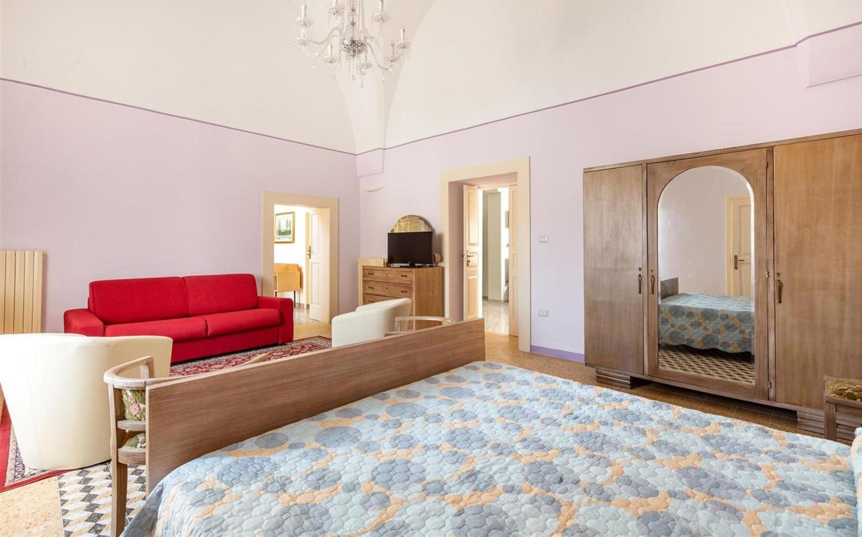 A bedroom with a bed, a red sofa, a wooden wardrobe, and a TV.