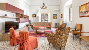 A spacious living room with a sofa, chairs, a TV, and a chandelier. - 2043 Antica Dimora Stasi by Barbarhouse (Presicce-Acquarica)