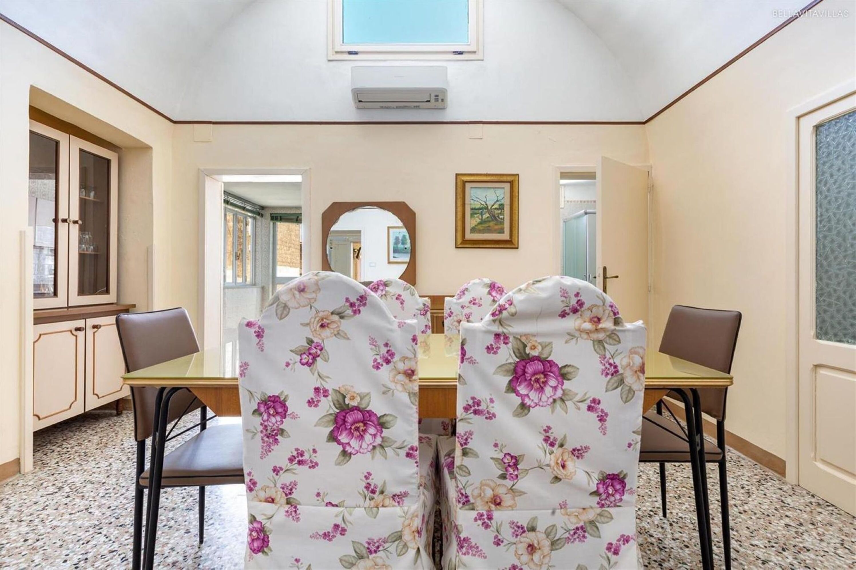 A dining area with a table and chairs, a mirror, and a window.