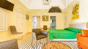 A hotel room with a bed, two chairs, a sofa, a round table, a chandelier, and artwork on the walls. - 2043 Antica Dimora Stasi by Barbarhouse (Presicce-Acquarica)