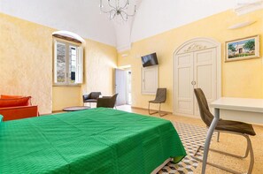 A room with a bed, a dining table, chairs, a TV, and a door. - 2043 Antica Dimora Stasi by Barbarhouse (Presicce-Acquarica)