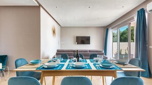 A dining area with a table set for four, blue chairs, a sofa, and a TV mounted on the wall. - 2055 Villa San Teodoro (Avetrana)