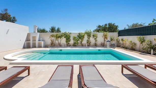 A rectangular swimming pool with a white deck, surrounded by lounge chairs and small trees. - 2055 Villa San Teodoro (Avetrana)