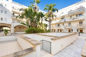Un patio con piscina, rodeado de edificios de varios pisos con balcones y un jardín central con palmeras.