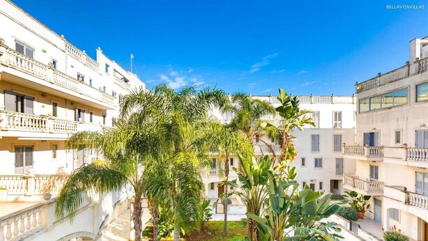 A courtyard with palm trees, a fountain, and multi-story buildings with balconies. - 2122 Appartamento Corso Italia II by Barbarhouse (Gallipoli)
