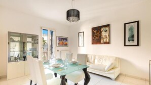 A dining area with a glass table, white chairs, a white sofa, and framed artwork on the walls. - 2122 Appartamento Corso Italia II by Barbarhouse (Gallipoli)