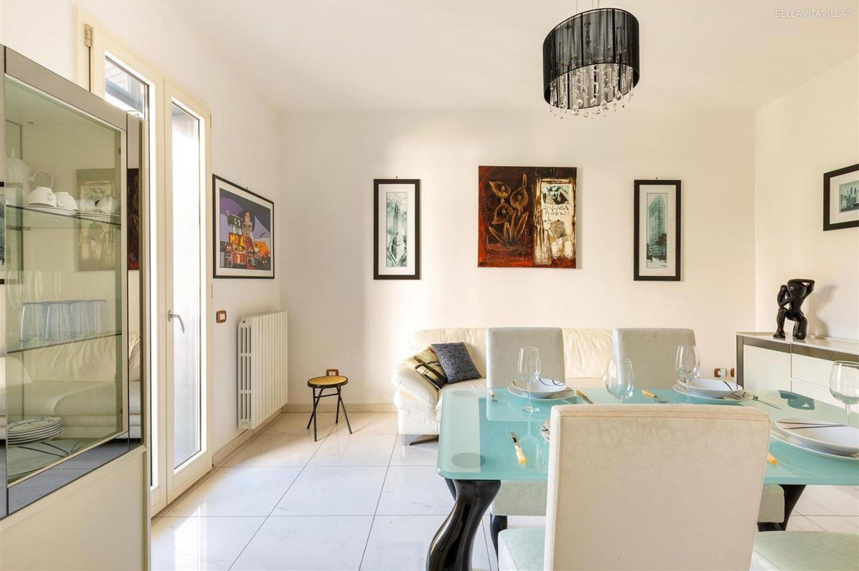 A dining area with a glass table, white chairs, and a chandelier.