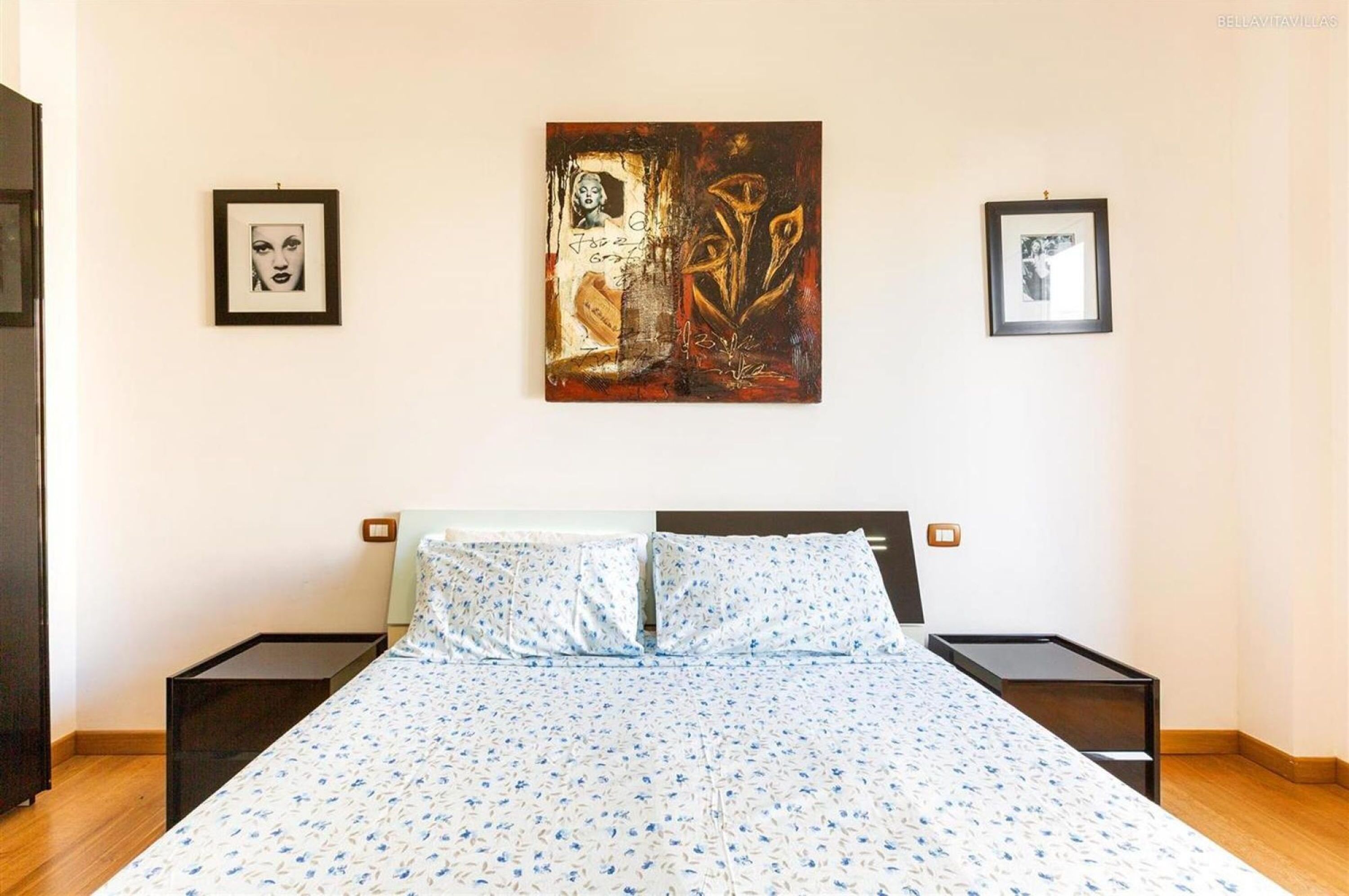 A bedroom with a bed, two nightstands, and two framed artworks on the wall.