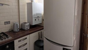 Eine kleine Küche mit weißen Fliesen im U-Bahn-Stil, einem eingebauten Toaster, einem Gasherd und einem weißen Kühlschrank.