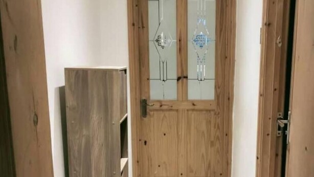 Eine Holztür mit Glasfeldern, ein Holzkabinett links und ein schmaler Flur.