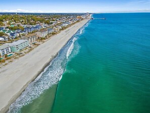 An aerial view of a coastal town with a beach, buildings, and a pier extending into the water. - Surfside Beach Family Retreat w/ Private Pool & 5BRs (Surfside Beach)
