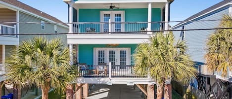 A two-story house with a balcony, a covered front porch, and palm trees.