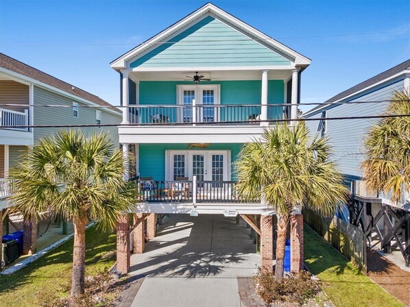 A two-story house with a balcony, a covered front porch, and palm trees. - Surfside Beach Family Retreat w/ Private Pool & 5BRs (Surfside Beach)