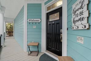 Une maison à l’extérieur turquoise, avec une porte noire, une pancarte d’accueil et une autre qui indique : « Qu’est-ce que c’est agréable d’être chez soi. »