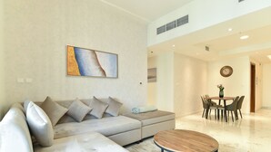 A modern living room with a sectional sofa, a round coffee table, and a dining area with a table and chairs. - Dubai Canal View 1 BR Premium Apartment - AMN (Dubai)