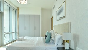A hotel room with a large bed, a nightstand with a lamp, a wardrobe, and a window with curtains. - Dubai Canal View 1 BR Premium Apartment - AMN (Dubai)