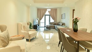 A spacious living area with a large wooden dining table, comfortable seating, and a view of a balcony. - Dubai Canal View 1 BR Premium Apartment - AMN (Dubai)