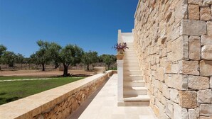 A stone pathway leading to a building with a stone wall and a view of trees and grass. - 496 La Serrazza in Pescoluse Posto Vecchio (Salve)