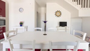 A dining area with a white table and chairs, a clock, a decorative sun-like wall piece, and a staircase.