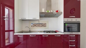 A kitchen with red cabinets, a white countertop, a gas stove, a built-in oven, and a window with a decorative grille.