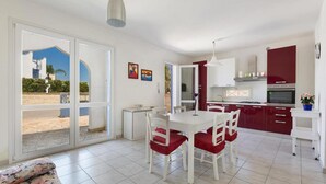 A modern kitchen with red cabinets, a white dining table with red chairs, and a large sliding glass door leading to an outdoor area.