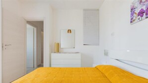 A bedroom with a bed, a dresser, a mirror, and a window with blinds.