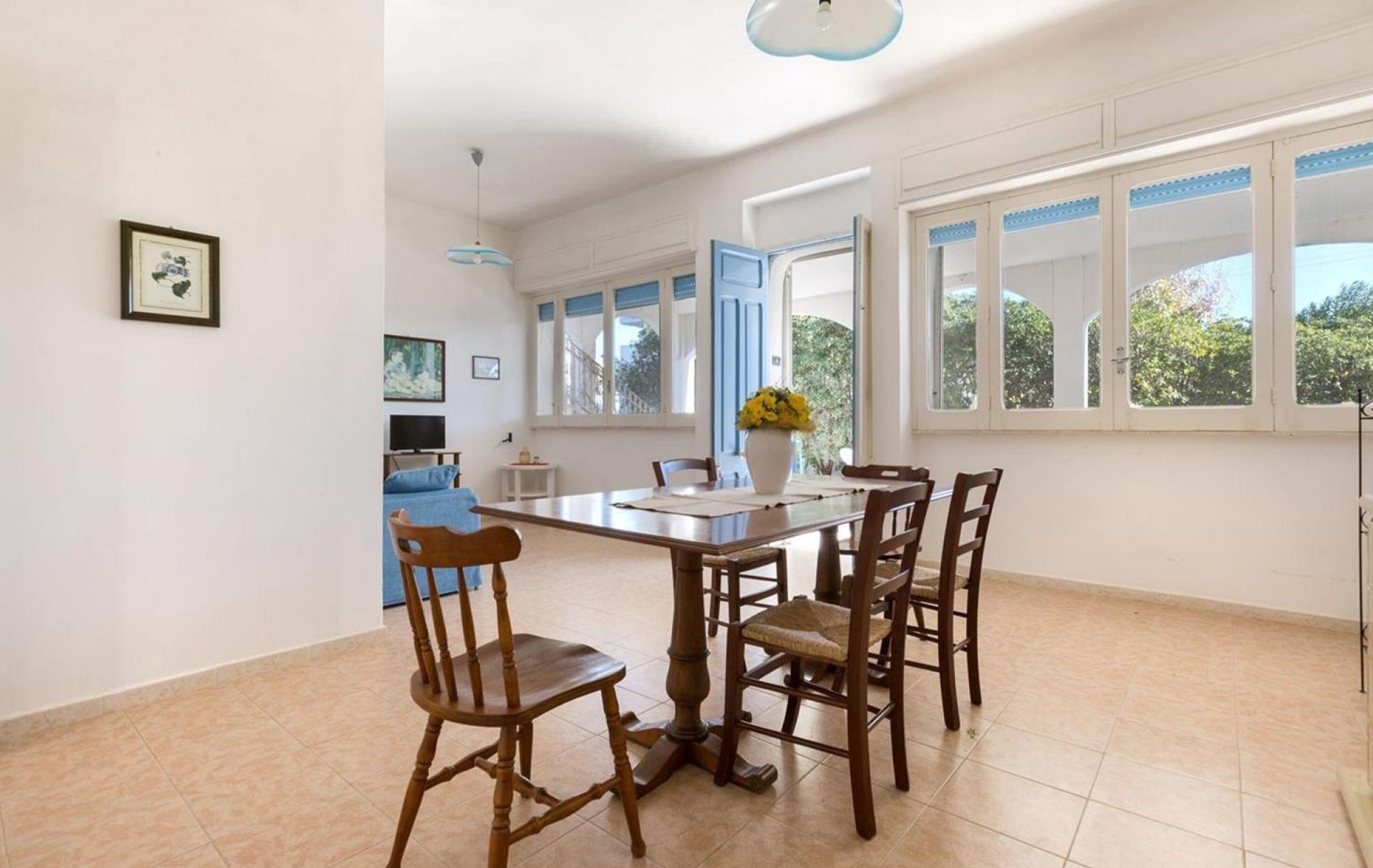 A dining area with a table and chairs, a blue sofa, and a window with a view of greenery.
