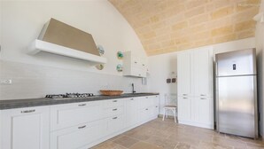 Una cocina con armarios blancos, un refrigerador de acero inoxidable y un piso de baldosas de piedra.