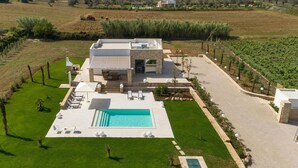 Una casa moderna con piscina, mobiliario exterior y un viñedo al fondo.