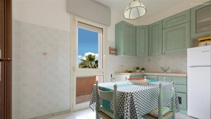 Une cuisine avec des armoires de couleur turquoise, un réfrigérateur blanc et une table recouverte d’une nappe à motifs géométriques.
