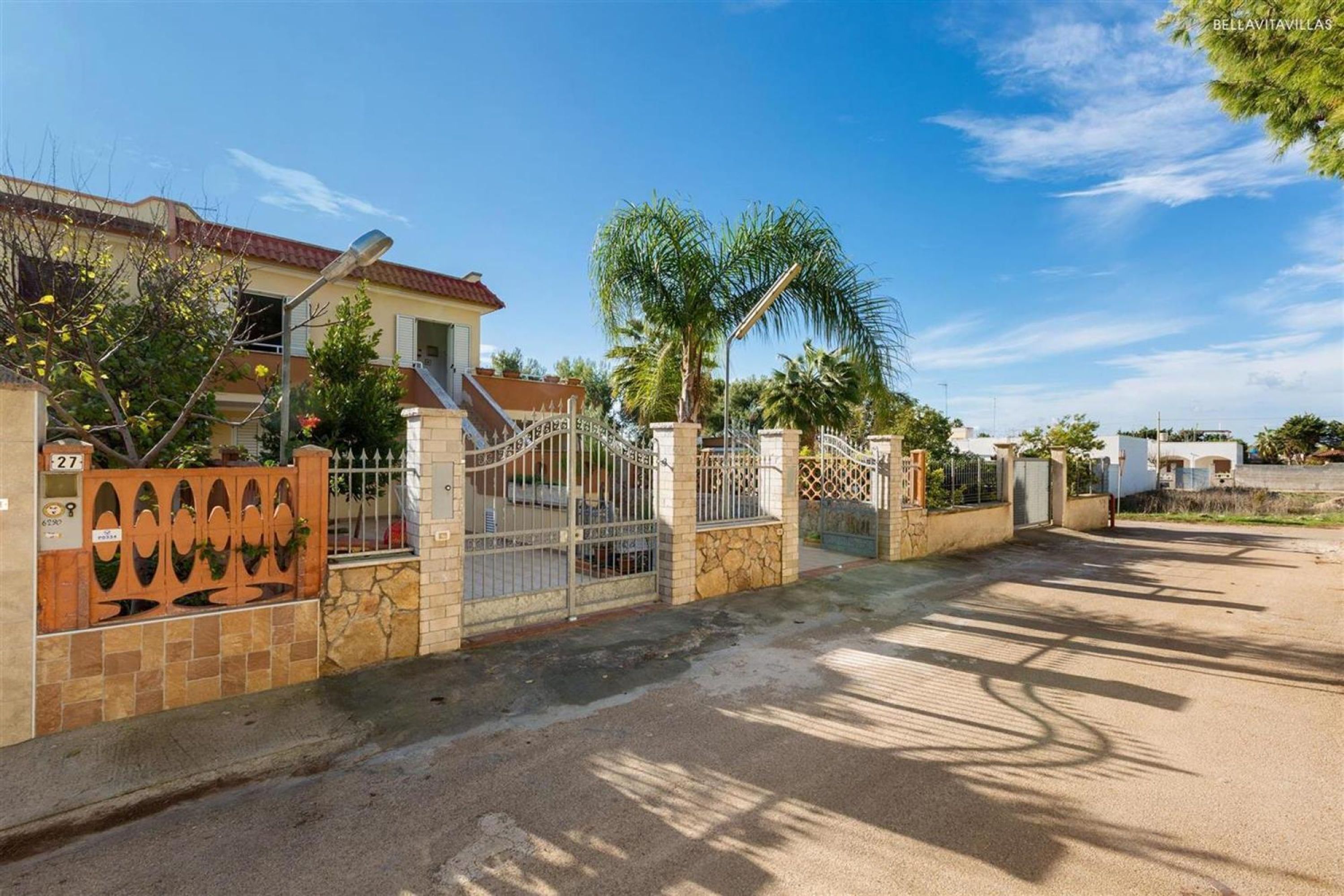 A gated residential area with a house, palm trees, and a clear sky.