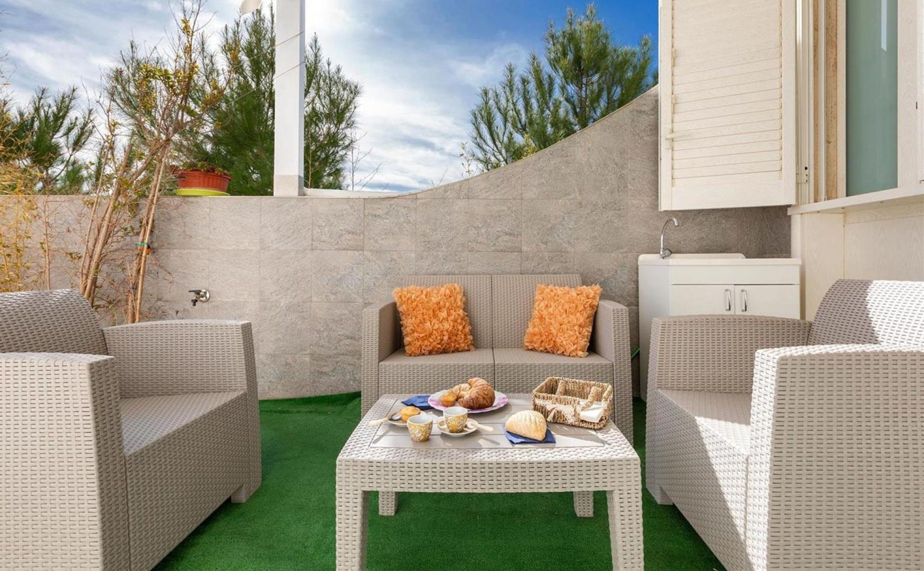 Un patio con mobiliario de mimbre, una mesa con comida y un armario blanco.