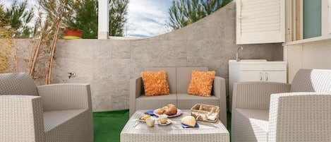 Un patio con mobiliario de mimbre, una mesa con comida y un armario blanco.