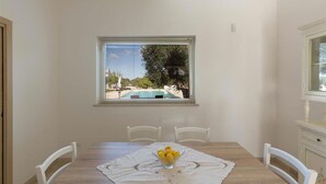 A dining area with a wooden table, white chairs, and a window with a view of a swimming pool.