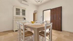 A dining area with a wooden table and white chairs, a white cabinet with glass doors, and a wooden door.