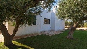 A white building with a small window, surrounded by a well-maintained lawn and two trees.