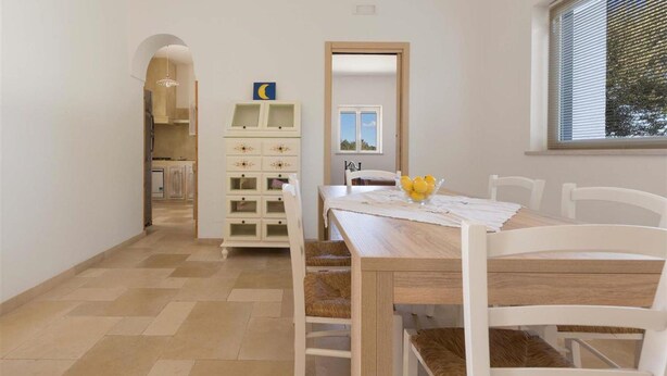 A dining area with a wooden table, white chairs, and a small cabinet with drawers.