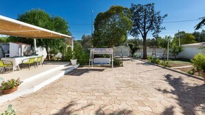 Ein überdachter Patio-Bereich mit Tisch, Stühlen, einer Schaukel und einer Pergola.