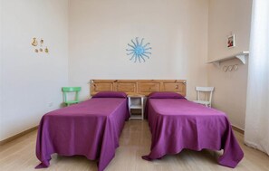 Una habitación con dos camas individuales, cabecero de madera, una mesita y una silla verde.