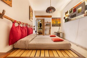 Un dormitorio pequeño con una cama plataforma de madera, un edredón rojo y beige, y un cabecero de madera original.