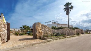 Ein Gebäude mit Steinmauern, einem gepflasterten Eingangsbereich, einer Palme und blauem Himmel.