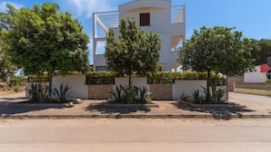Un edificio moderno con fachada blanca, rodeado de un jardín ajardinado con varios árboles y plantas.