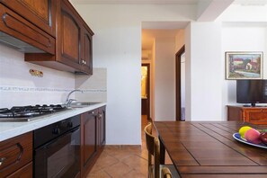 A kitchen with wooden cabinets, a gas stove, and a dining area with a table and chairs. - 2404 Villa Cieloazzurro - Bilo by Barbarhouse (Nardò)