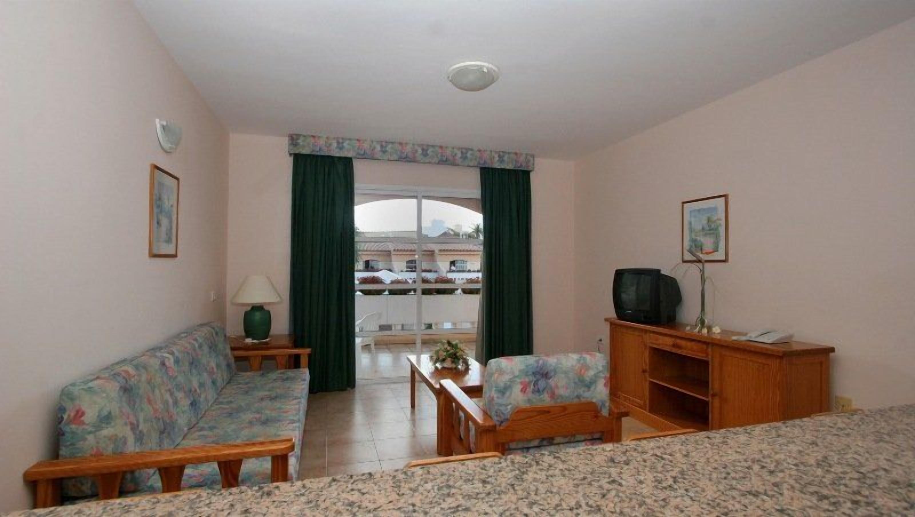 Una sala de estar con un sofá, una mesa de centro, un mueble para televisión y vistas a través de una ventana.
