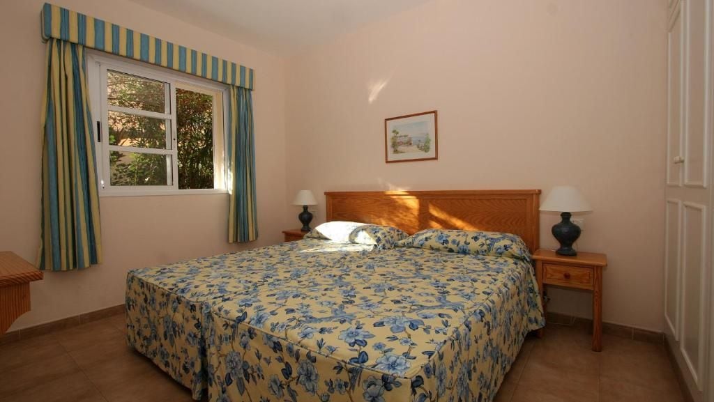 A bedroom with a bed, two bedside tables, a window with curtains, and a wall-mounted picture.