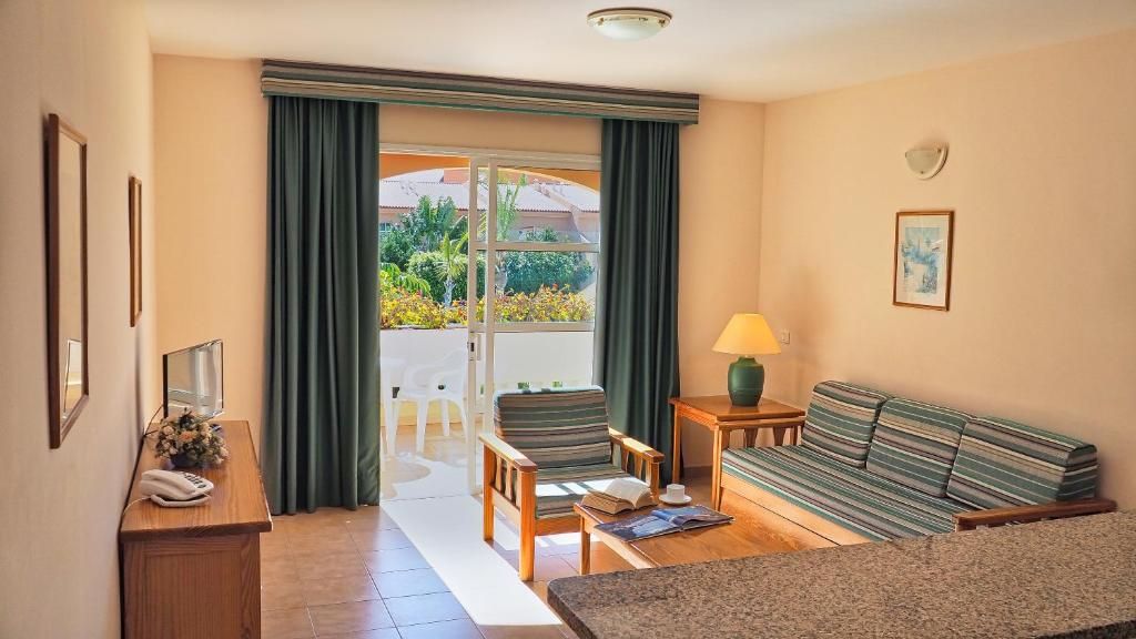 Quarto de hotel com sofá, uma mesa pequena, abajur, telefone e vista para o exterior através de uma porta de vidro.