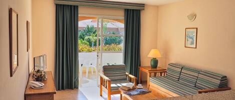Quarto de hotel com sofá, uma mesa pequena, abajur, telefone e vista para o exterior através de uma porta de vidro.
